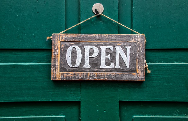 Sign hung on dark green front door stating 'Open'.  